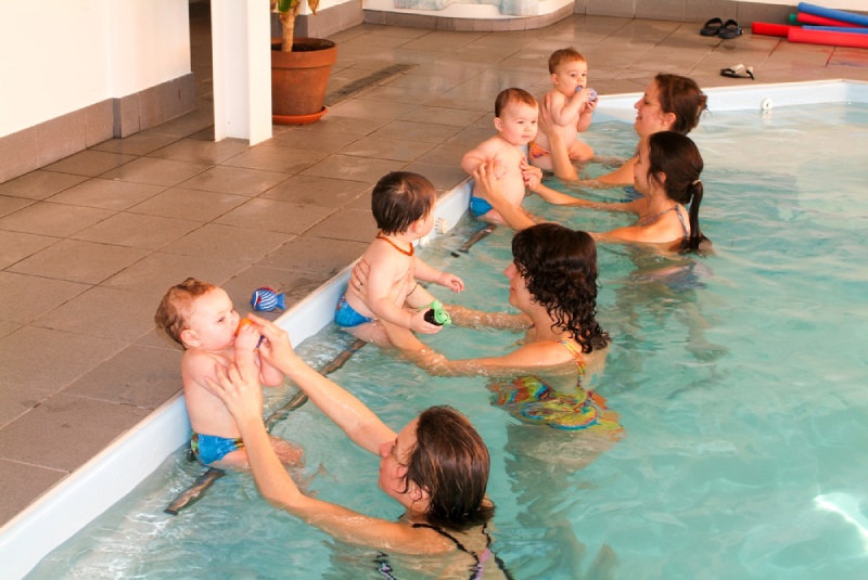 Benefits of Early Swimming Education: Adorable babies enjoying swimming in a pool in Switzerland with with their relatives, early development class for infants teaching children to swim and dive